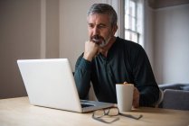 Mann schaut auf Laptop, während er zu Hause Kaffee trinkt — Stockfoto