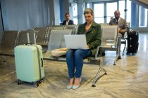 Жінка з багажем за допомогою ноутбука в зоні очікування в терміналі аеропорту — стокове фото