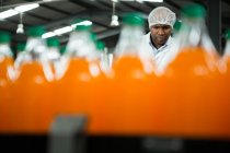 Trabajador masculino serio visto a través de botellas de jugo de naranja en fábrica - foto de stock