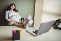 Femme d'affaires enceinte se détendre avec les pieds dans le bureau — Photo de stock