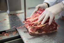 Nahaufnahme eines Metzgers, der rohes Fleisch auf Bandsägemaschine in Fleischfabrik schneidet — Stockfoto