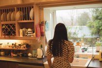 Задній вид жінка дивлячись через вікно кухні в домашніх умовах — стокове фото
