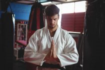Reproductor de karate en pose de oración en gimnasio - foto de stock