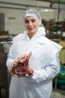 Retrato de una carnicera sosteniendo carne en una fábrica de carne - foto de stock