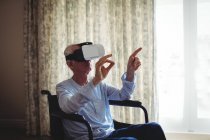 Uomo anziano seduto sulla sedia a rotelle e utilizzando cuffie realtà virtuale in camera da letto a casa — Foto stock