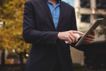 Mid section of businessman holding mobile phone and using digital tablet on street — Stock Photo