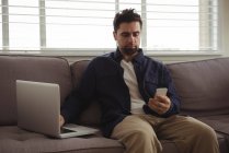 Людина за допомогою мобільних телефонів і ноутбуків на дивані в домашніх умовах — стокове фото