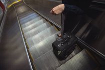 Low section of businesswoman with luggage standing on escalator — Stock Photo