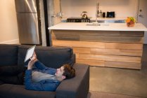 Улыбающийся мужчина лежит на диване, используя цифровой планшет в гостиной дома — стоковое фото