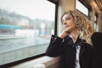 Mujer de negocios reflexiva mirando por la ventana mientras viaja - foto de stock