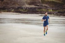 Atleta bonito correndo na praia arenosa — Fotografia de Stock