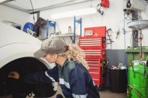 Mécanicien féminin examinant un frein à disque de roue de voiture dans le garage de réparation — Photo de stock