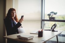 Embarazada mujer de negocios utilizando el teléfono móvil en la oficina - foto de stock