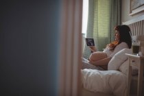 Mujer embarazada mirando una sonografía en la mesa digital en el dormitorio - foto de stock