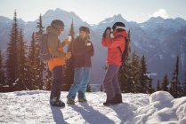 Esquiadores interactuando entre sí mientras toman tazas de café en montañas cubiertas de nieve - foto de stock