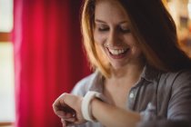 Sorrindo mulher verificando seu smartwatch em casa — Fotografia de Stock