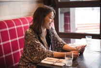 Mujer sentada en el restaurante y usando una tableta digital - foto de stock
