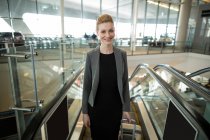 Businesswoman standing near escalator with luggage at airport — Stock Photo