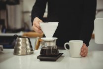 Mittelteil des Mannes mit Filtertrichter und Kaffeetasse im Coffeeshop — Stockfoto