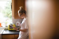 Жінка використовує цифровий планшет, маючи каву на кухні вдома — стокове фото