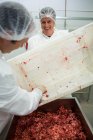Butchers emptying tray with minced meat at meat factory — Stock Photo