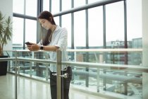 Businesswoman leaning on railing and using mobile phone at office corridor — Stock Photo