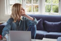 Femme réfléchie utilisant un ordinateur portable dans le salon à la maison — Photo de stock