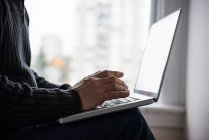 Sección media del hombre sentado en la cama y usando el ordenador portátil en casa - foto de stock