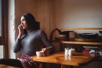 Woman talking on mobile phone while having cup of coffee in cafe — Stock Photo