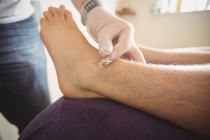 Крупним планом фізіотерапевт, що виконує сухе плетіння на нозі пацієнта в клініці — стокове фото
