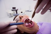 Dentista examinando paciente femenina con herramientas en clínica dental - foto de stock