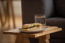 Сендвіч на тарілці зі склянкою води на табуреті в домашніх умовах — стокове фото