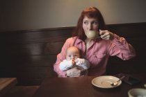 Mother having coffee while holding cute baby in cafe — Stock Photo