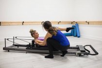 Mulher treinadora auxiliando mulher com exercício de alongamento no reformador no ginásio — Fotografia de Stock