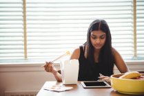 Frau nutzt digitales Tablet beim Essen mit Essstäbchen zu Hause — Stockfoto