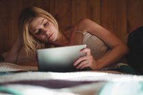 Женщина лежит на кровати и пользуется цифровым планшетом в спальне дома — стоковое фото