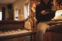 Женщина с помощью мобильного телефона во время кофе на кухне — стоковое фото
