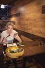 Mulher usando telefone celular enquanto come sushi no restaurante — Fotografia de Stock