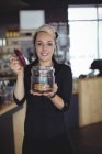 Портрет офіціантки, що тримає банку печива за лічильником в кафе — стокове фото