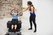 Female trainer assisting woman with exercising with pilates ring in gym — Stock Photo