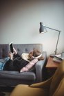 Donna sdraiata sul divano ad ascoltare musica su tablet digitale a casa — Foto stock
