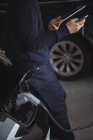 Mid section of man using digital tablet and mobile phone while charging electric car in garage — Stock Photo