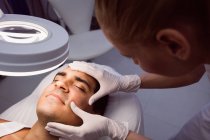 Médico examinando rosto masculino para tratamento cosmético na clínica — Fotografia de Stock
