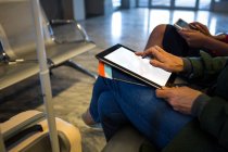 Sección media de la mujer que usa tableta digital en la sala de espera en el aeropuerto - foto de stock