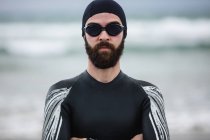 Спортсмен в мокром костюме стоит со скрещенными руками на пляже — стоковое фото