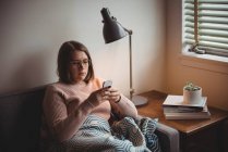 Frau sitzt mit Handy zu Hause auf Sofa — Stockfoto