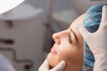 Manos del médico examinando la cara femenina para el tratamiento cosmético en la clínica - foto de stock