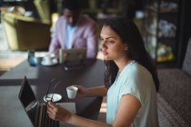 Задумчивая деловая женщина с чашкой кофе сидит за своим столом в офисе — стоковое фото