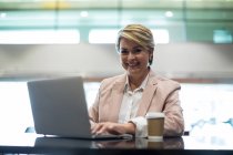 Retrato de mulher de negócios sorridente usando laptop na área de espera no terminal do aeroporto — Fotografia de Stock