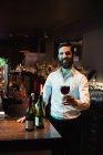 Retrato de barman segurando copo de vinho tinto no balcão de bar — Fotografia de Stock
